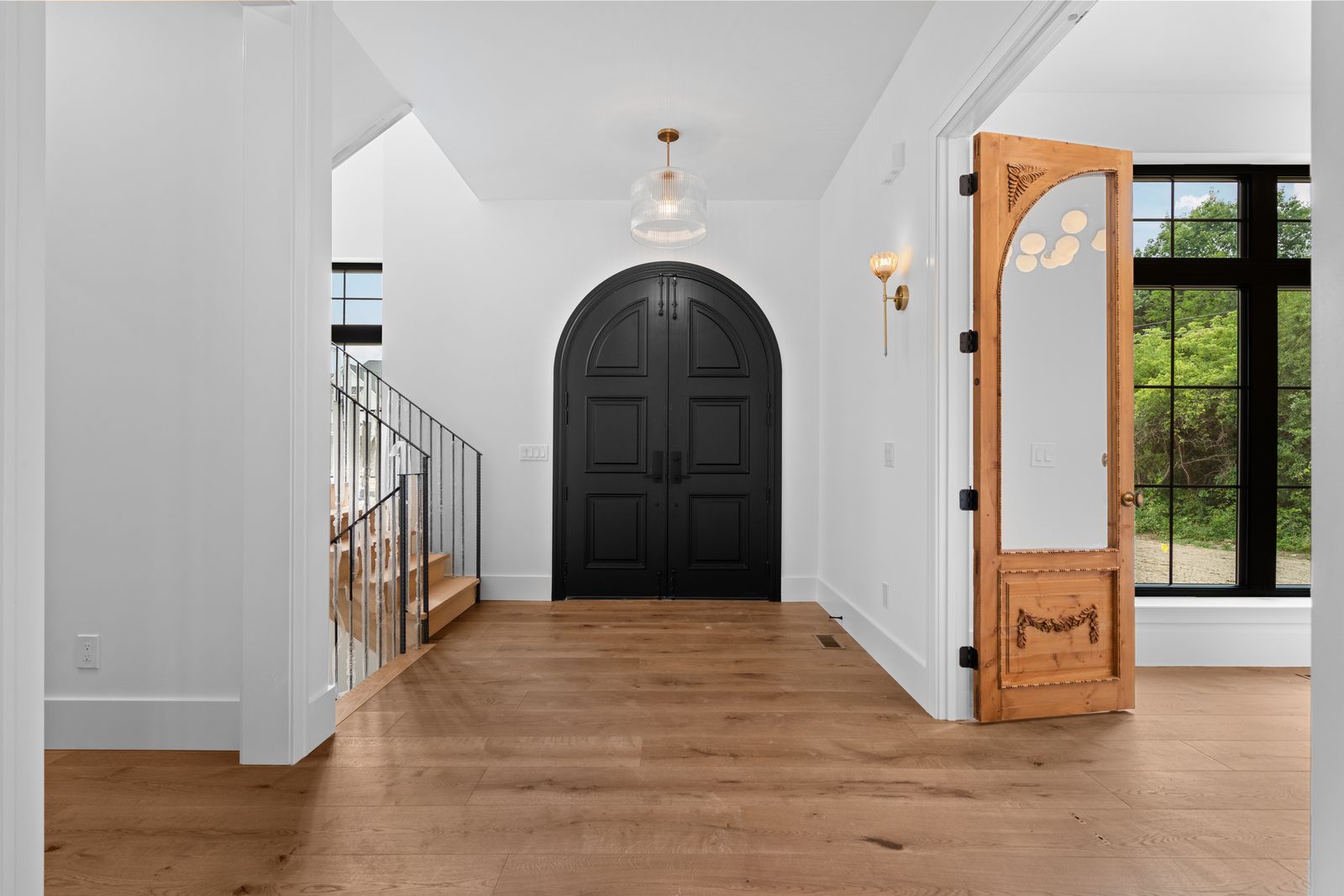 Entry foyer with arched walnut door and staircase